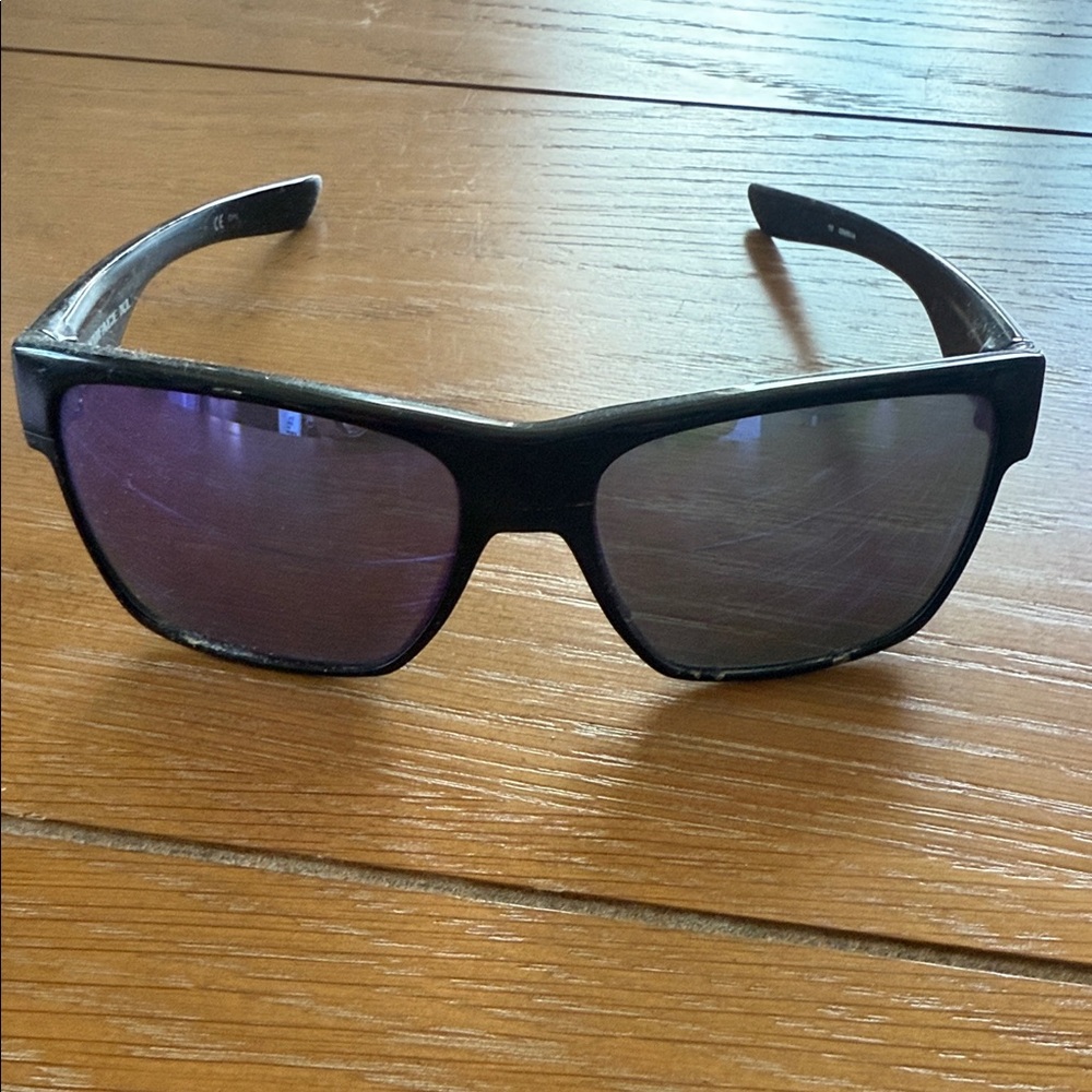 Oakley. Black sunglasses, purple lenses. Purple symbol on arm.